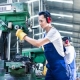 Factory worker operating a drilling machine with safety equipment in an industrial workshop
