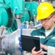 Engineer in safety helmet using a laptop to monitor and control industrial machinery in a manufacturing facility