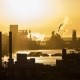 Industrial landscape at sunset with factories, chimneys, and smoke rising into the sky