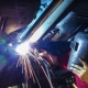 Welder wearing a protective helmet using a welding machine, with sparks flying in a factory